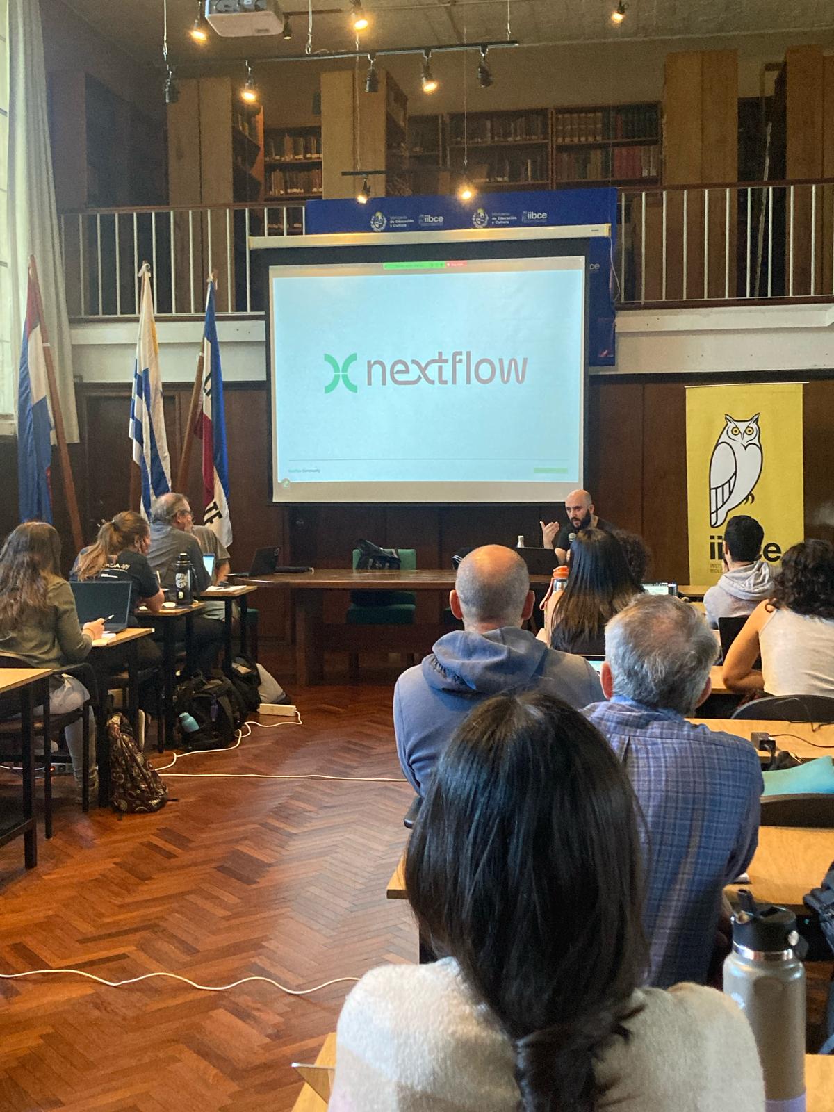 A picture from the workshop room, with the participants looking at the screen and myself presenting. The monitor says Nextflow.