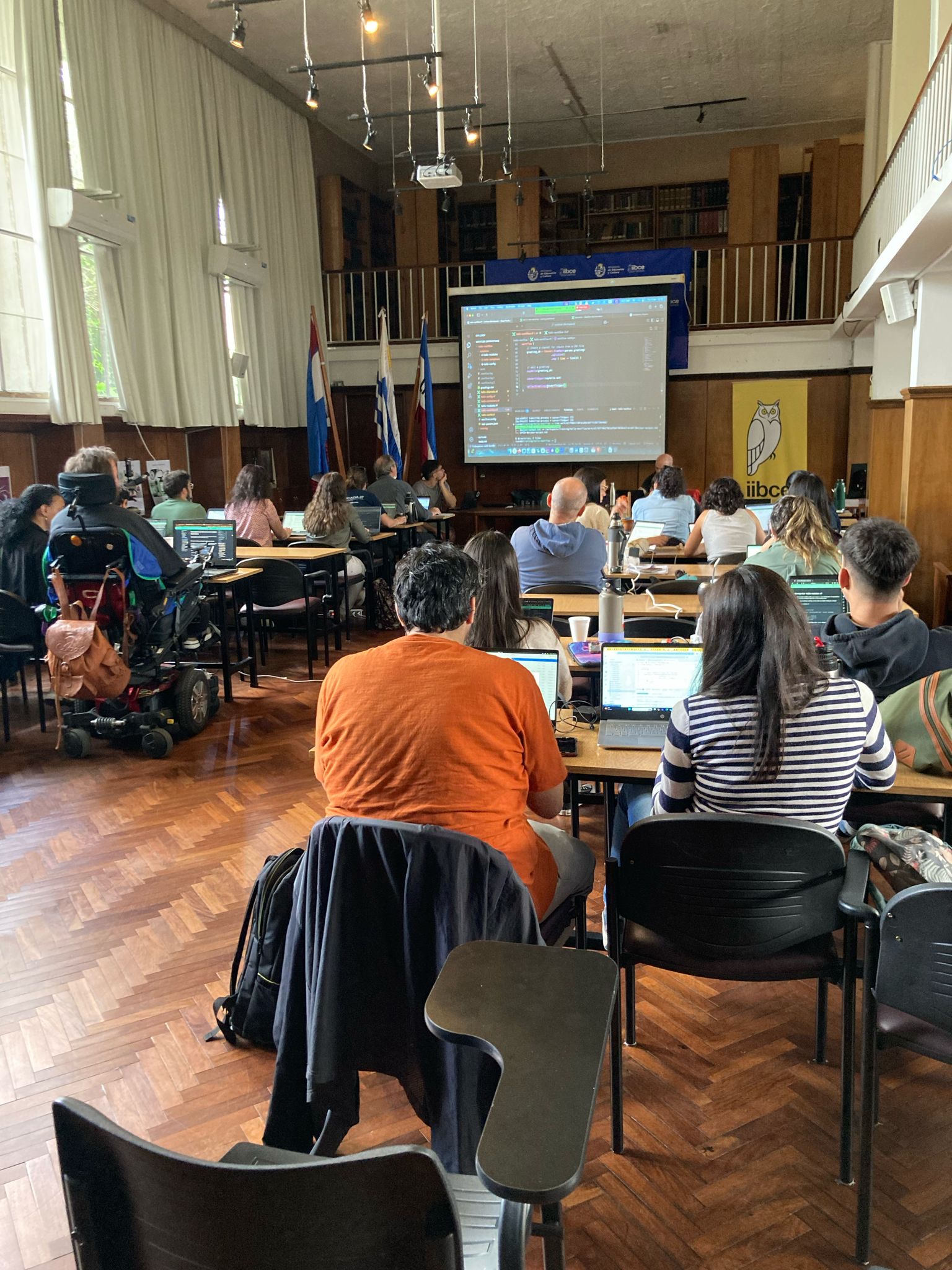 A picture from the workshop room, with the participants looking at the screen and myself presenting.